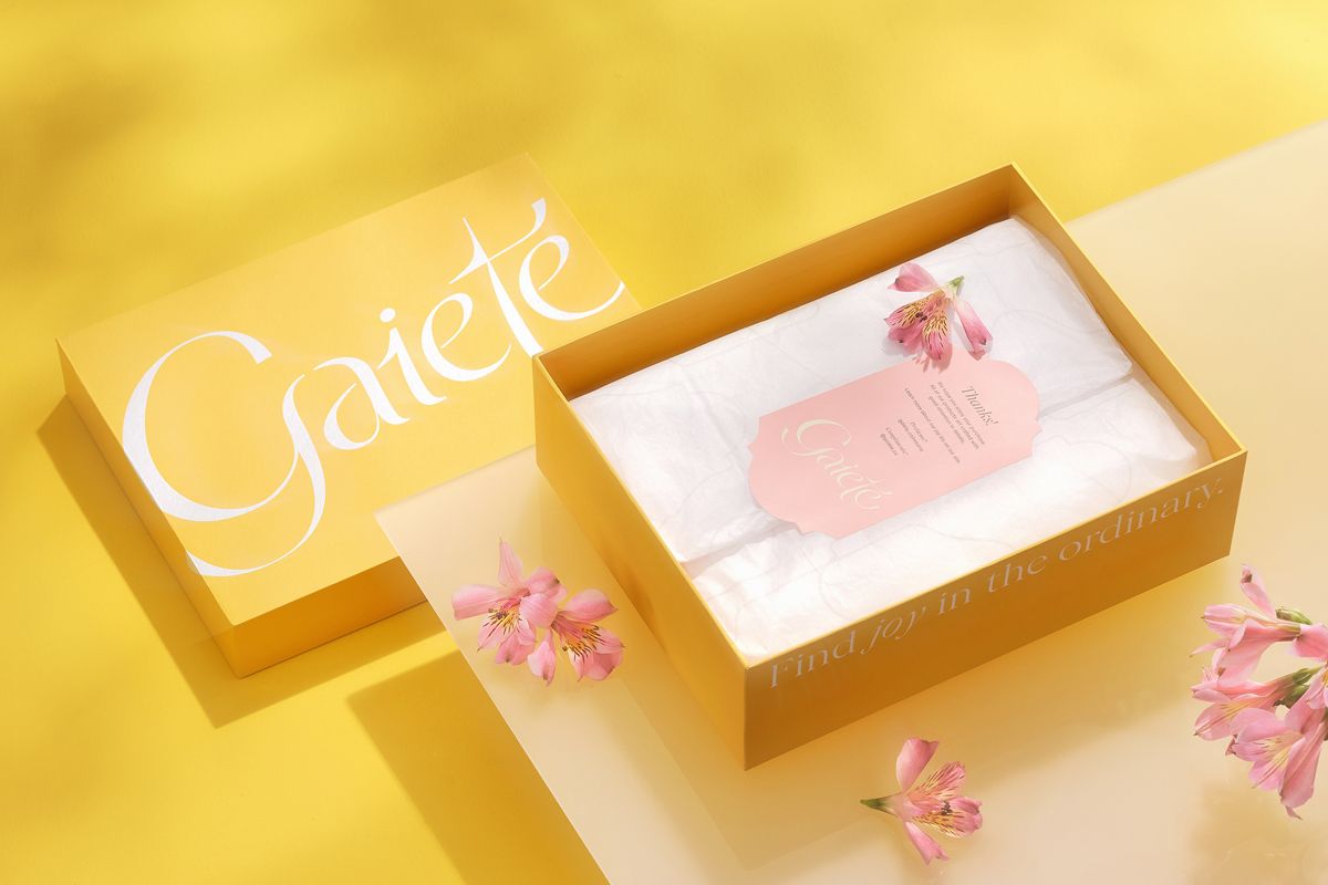 An opened two-piece box with a clothing packaging design applied on it and with wrapping paper and a greeting card inside the box.