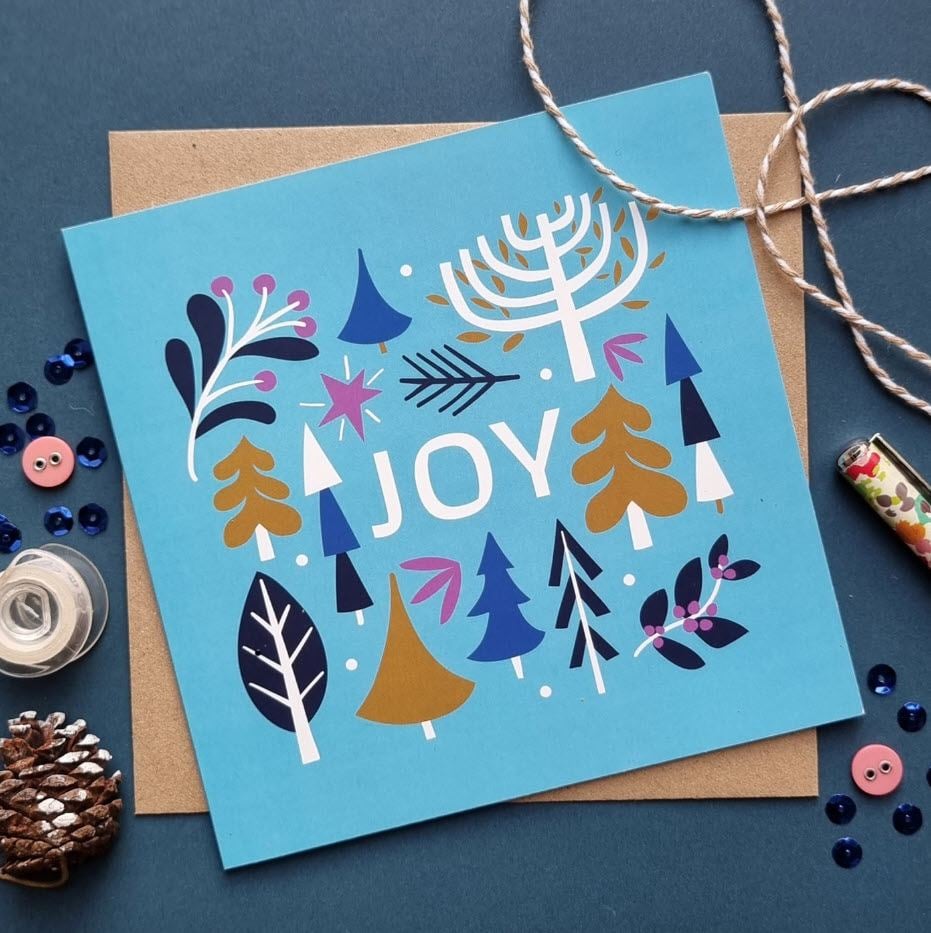Holiday card on top of a kraft paper envelope with rope, buttons and a pencil around.